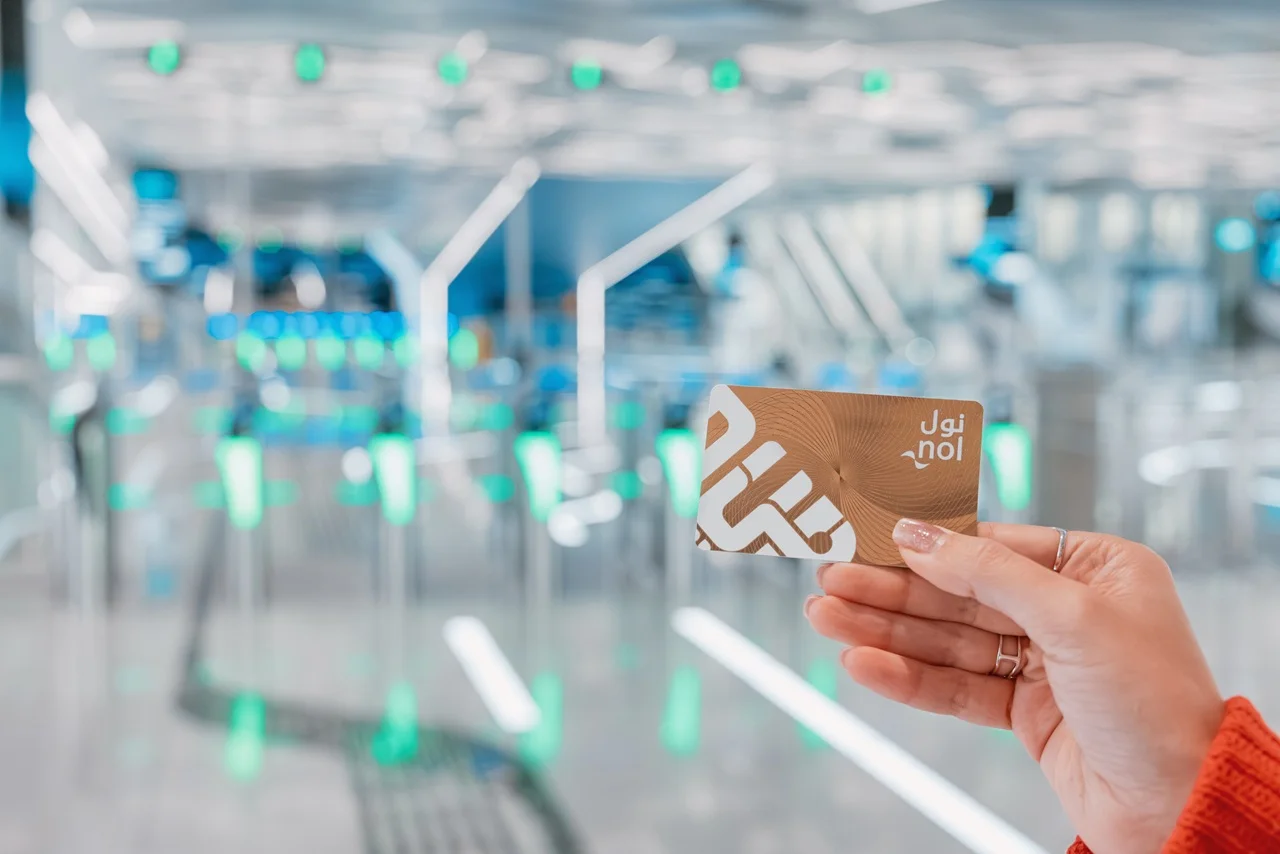 Dubai Nol Card Guide for Tourists: Types, Benefits & Top-Up Tips 4 A hand holds a Nol card in a bright transit station with green-lit turnstiles. The scene conveys modernity and efficient urban transport.