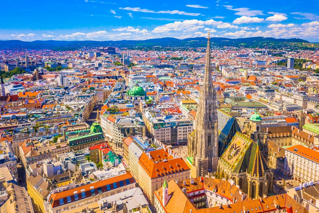 Austria Tourist Visa for UAE Residents: Complete 2026 Travel Guide 12 Aerial view of Vienna showcasing St. Stephen's Cathedral with its tall spire and colorful tiled roof amidst a cityscape of historic buildings under a blue sky.