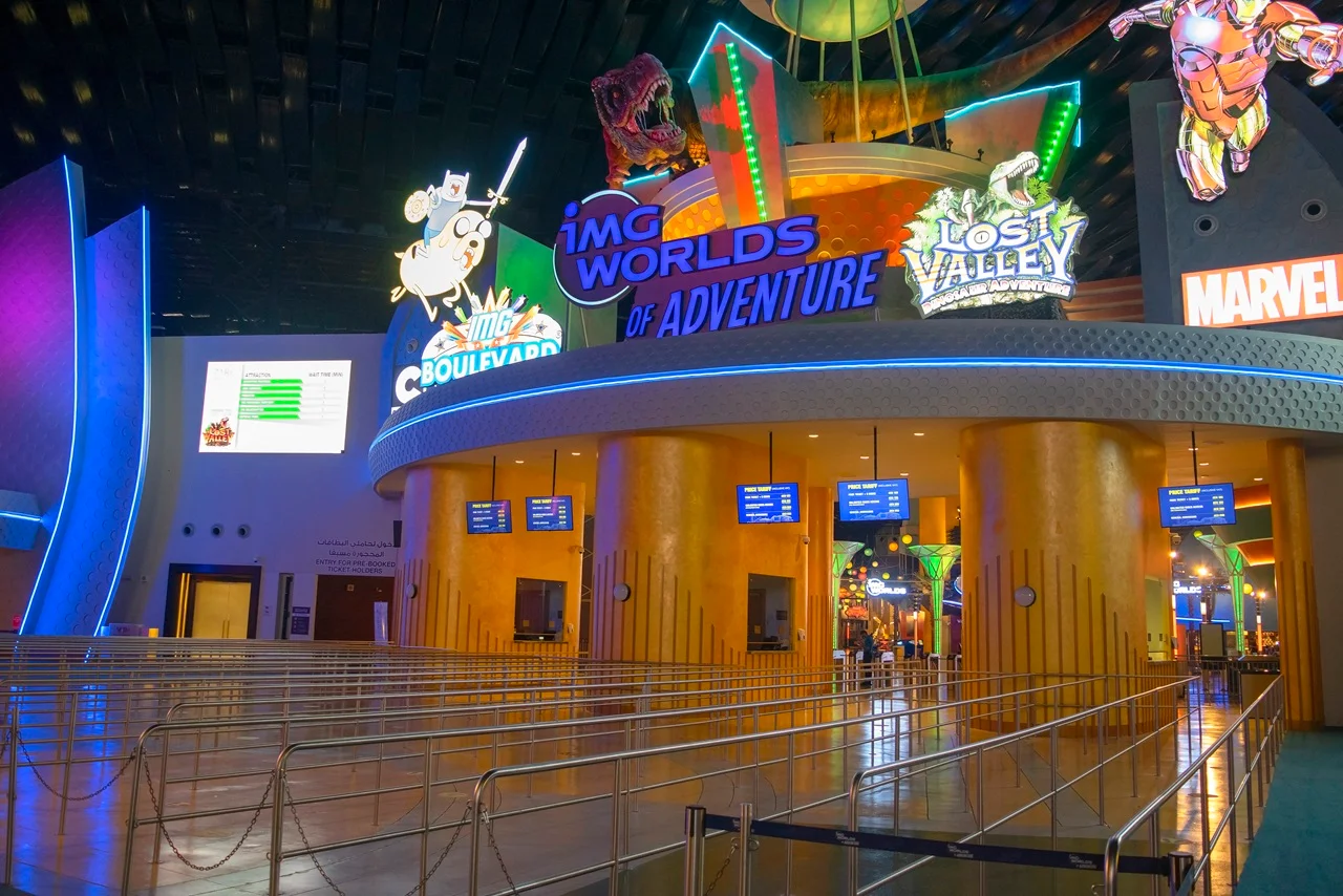 Brightly lit amusement park entrance at IMG Worlds of Adventure, featuring colorful signs for themed areas like Marvel and Lost Valley.