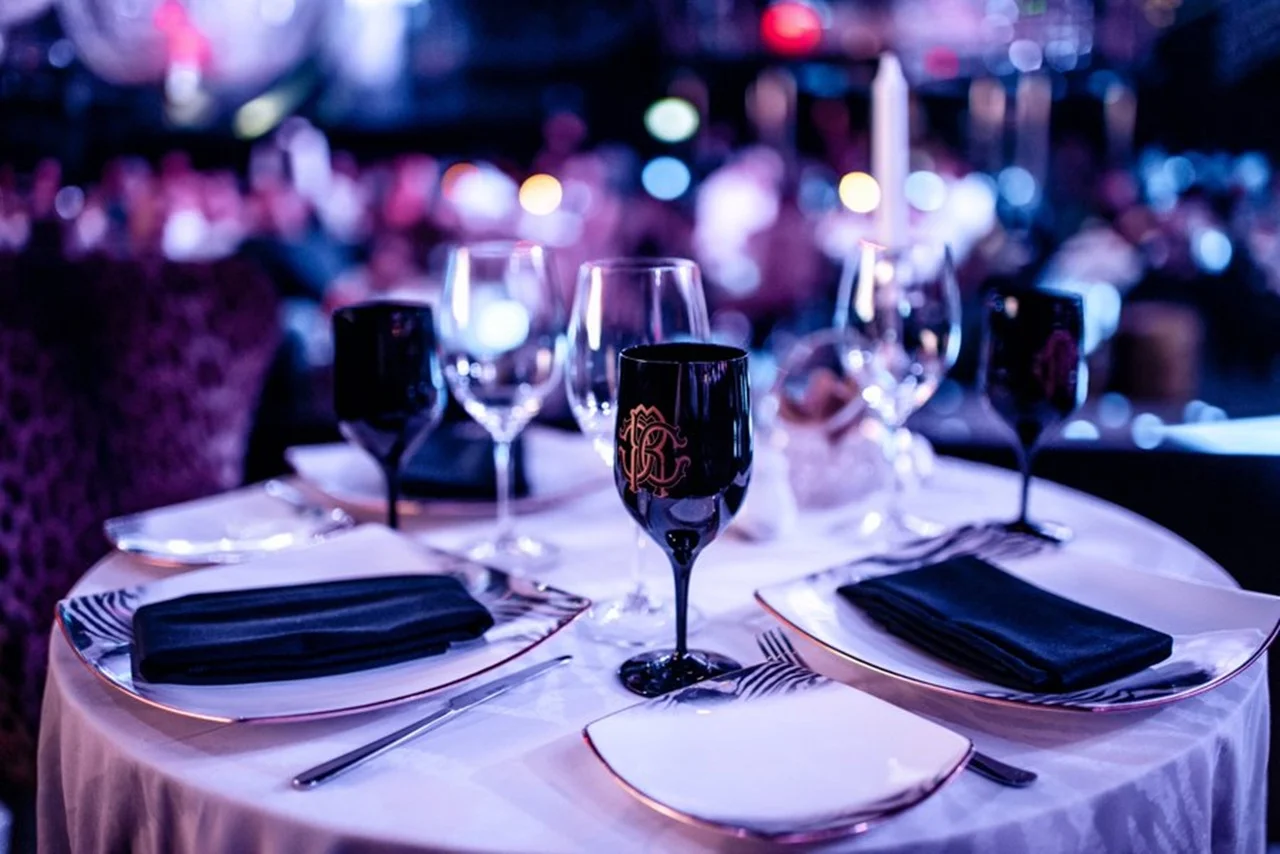Cavalli Club Dubai 35 Elegantly set dining table with black goblets, white plates, and black napkins in a dimly lit, upscale restaurant, creating a sophisticated ambiance.