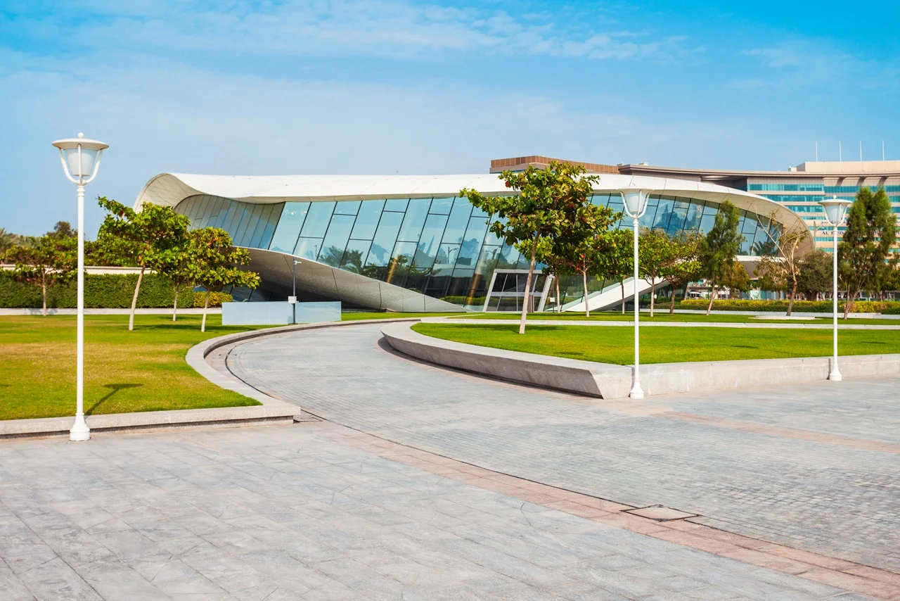 Explore the history of UAE; Etihad Museum speaks about where the nation was born 7 Modern building with curved glass facade set against a blue sky. Surrounded by green lawns and trees, with a winding pathway and white street lamps. Etihad Museum.