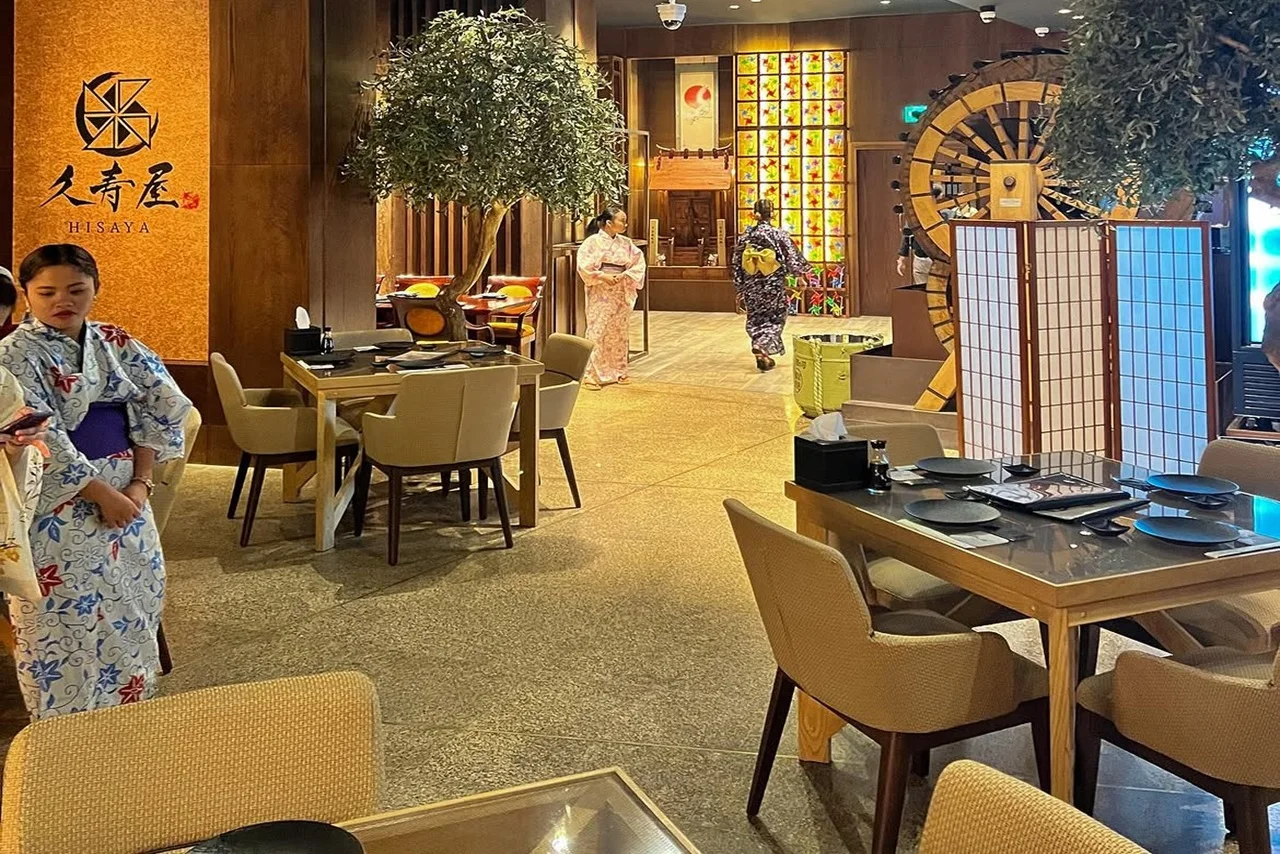 Taste Japan’s tradition: Dubai’s First Potage Ramen & A5 Wagyu at HISAYA Japanese Restaurant 9 A cozy Japanese restaurant with women in kimonos. Wooden decor, lit panels, and dining tables set the scene. Atmosphere is warm and inviting.