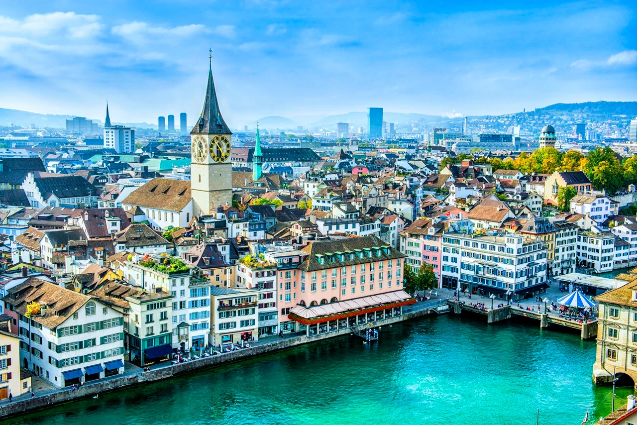 Switzerland Schengen Visa for UAE Residents: Complete 2026 Application Guide 9 Aerial view of Zurich, showing the historic city center with a prominent clock tower, colorful buildings, and a turquoise river under a clear blue sky.