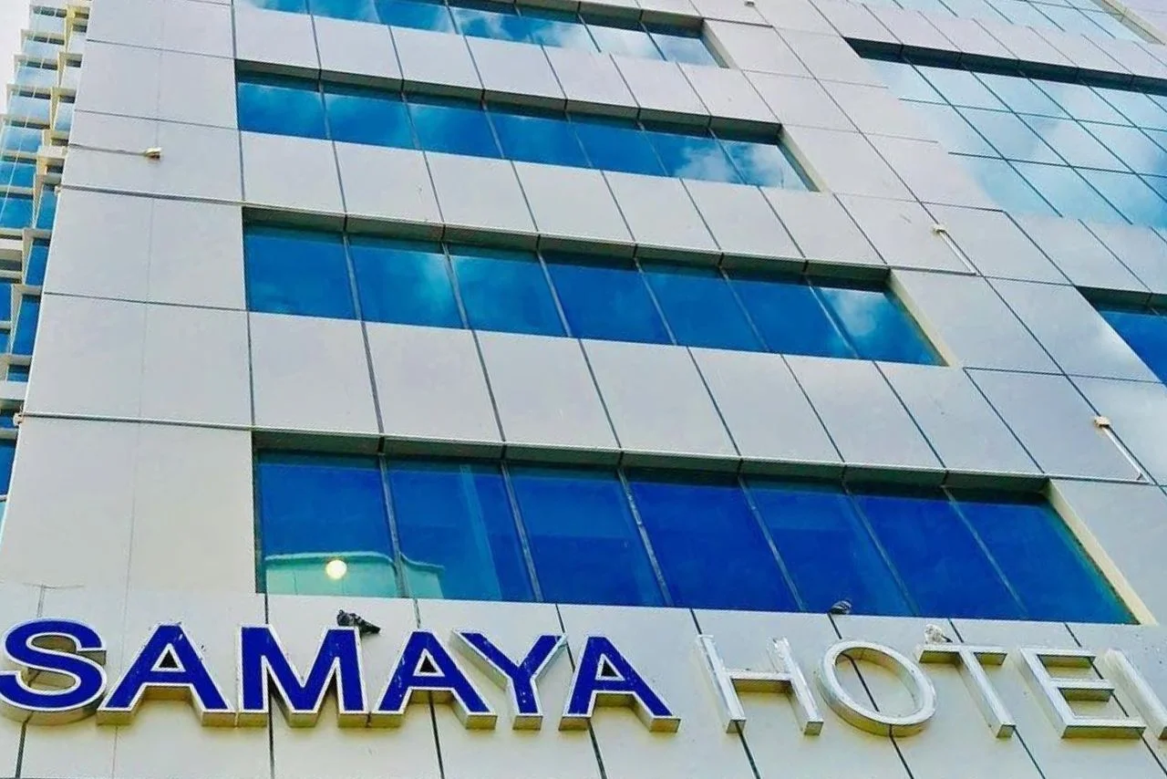 Close-up exterior view of the Samaya Hotel building showing rows of blue tinted windows reflecting the sky and large prominent signage on a white panel structure.